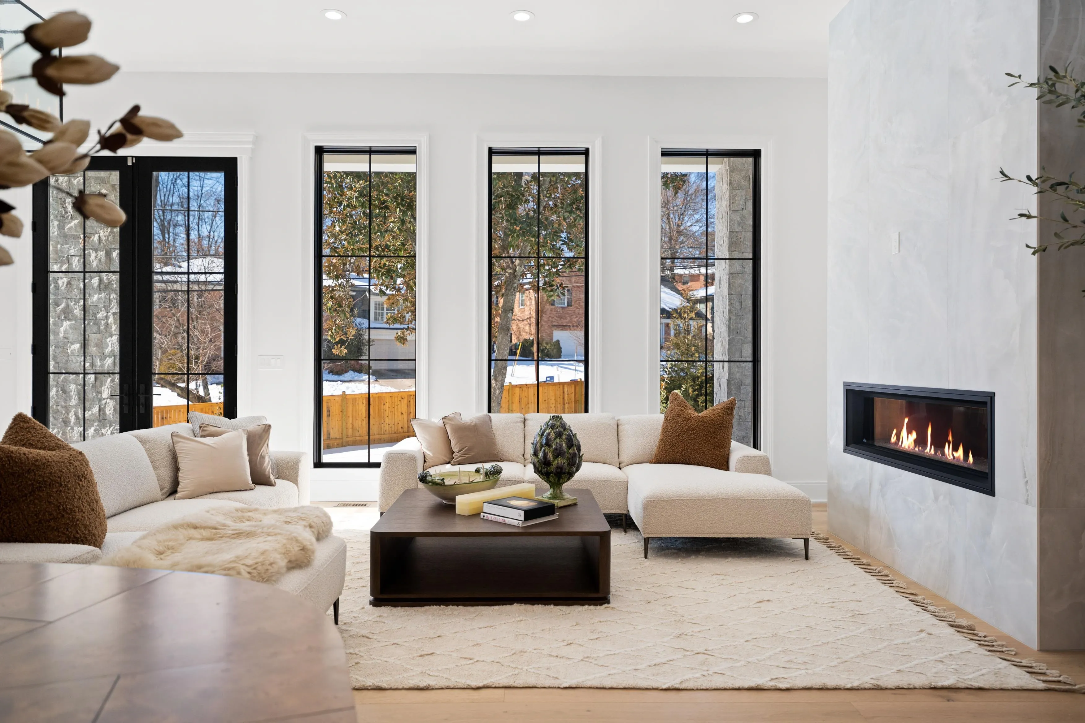 Living room with floor-to-ceiling black-framed windows, linear gas fireplace, and designer furniture