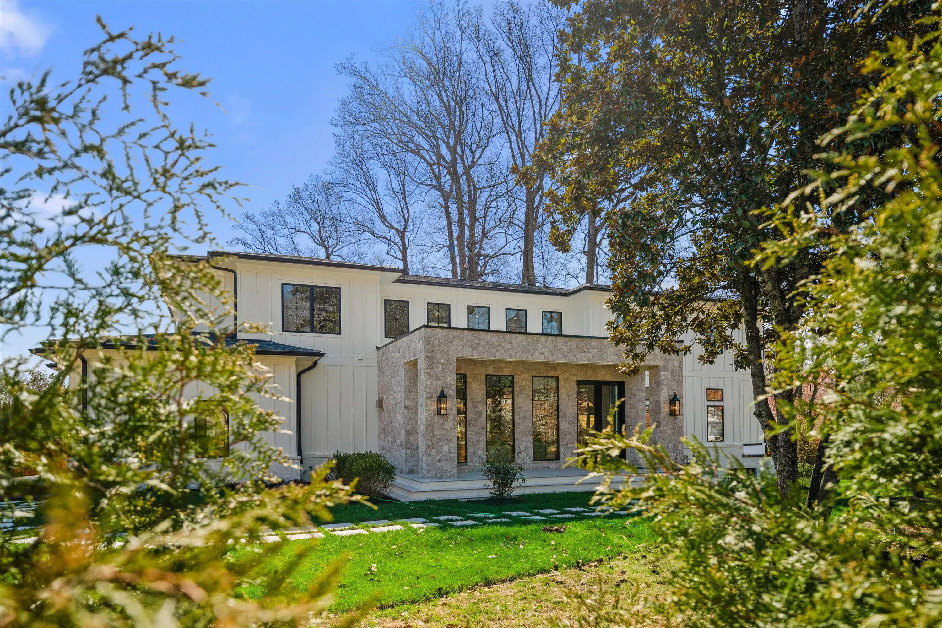 Front entrance with two-story stone-clad portico, board-and-batten siding, and modern lanterns framed by mature landscaping in Bethesda MD
