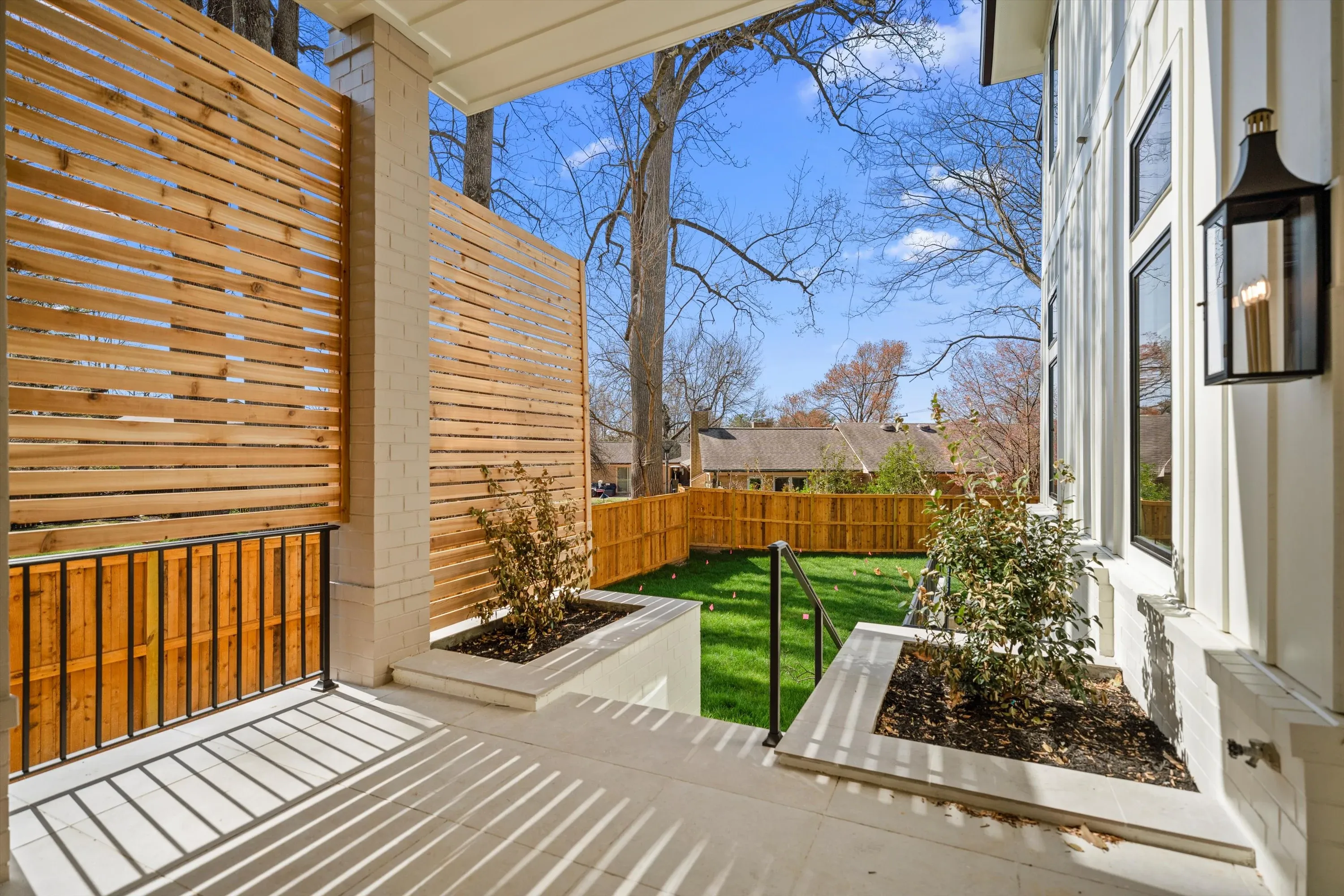Covered side porch with cedar privacy screen, tongue-and-groove ceiling, and gas lantern overlooking landscaped yard