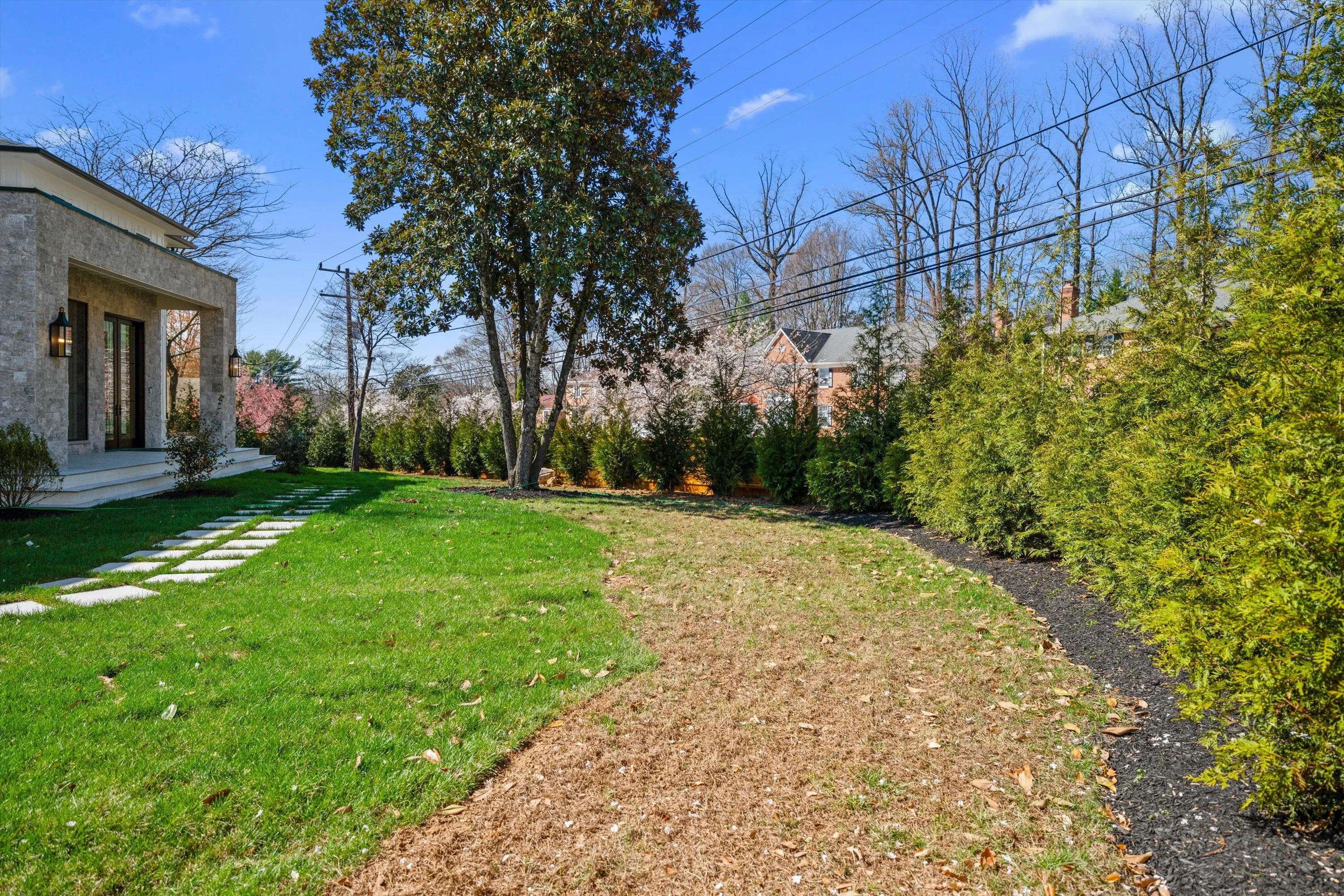 Side yard with stone-clad garden room, mulched planting beds, and pruned hedges along the property line