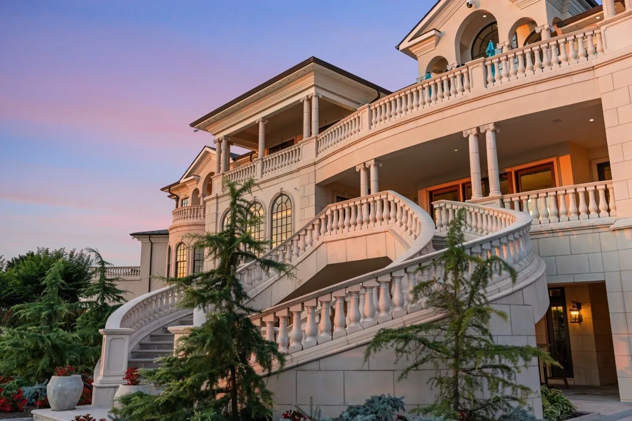 Luxury mansion exterior at sunset with illuminated windows and curved stone staircase