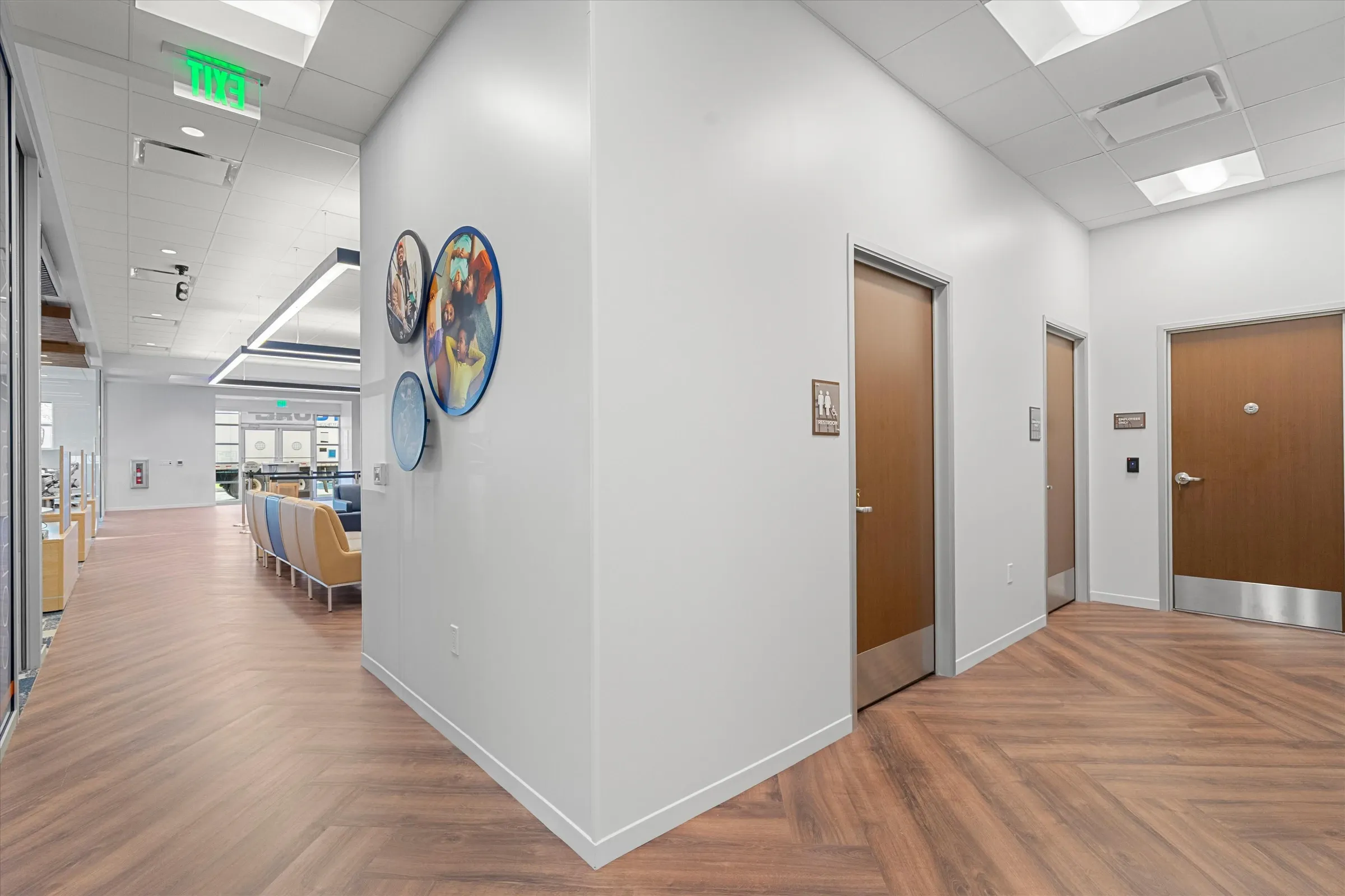 Branch hallway with herringbone wood flooring, circular branded military family artwork, restroom doors, and view into main lobby area