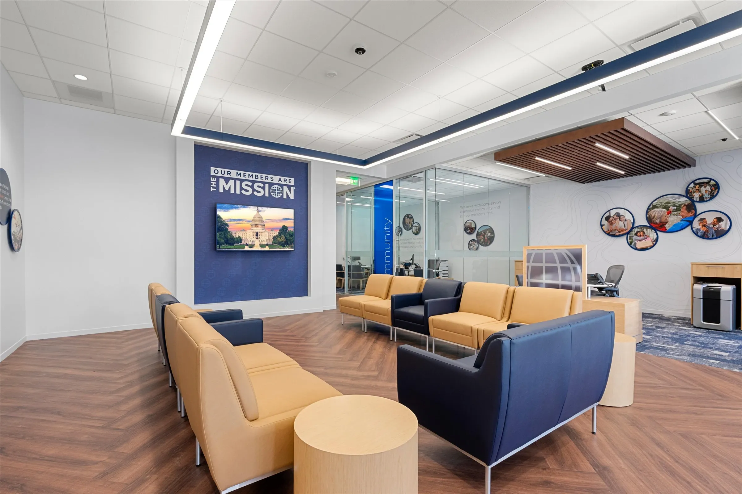 Member waiting area with navy and gold upholstered seating, "Our Members Are The Mission" Capitol display, circular military family photos, and glass consultation room