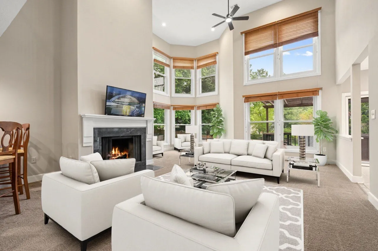 Virtually staged living room with white sectional sofa, stone fireplace, and floor-to-ceiling bay windows — virtual staging by Umedia