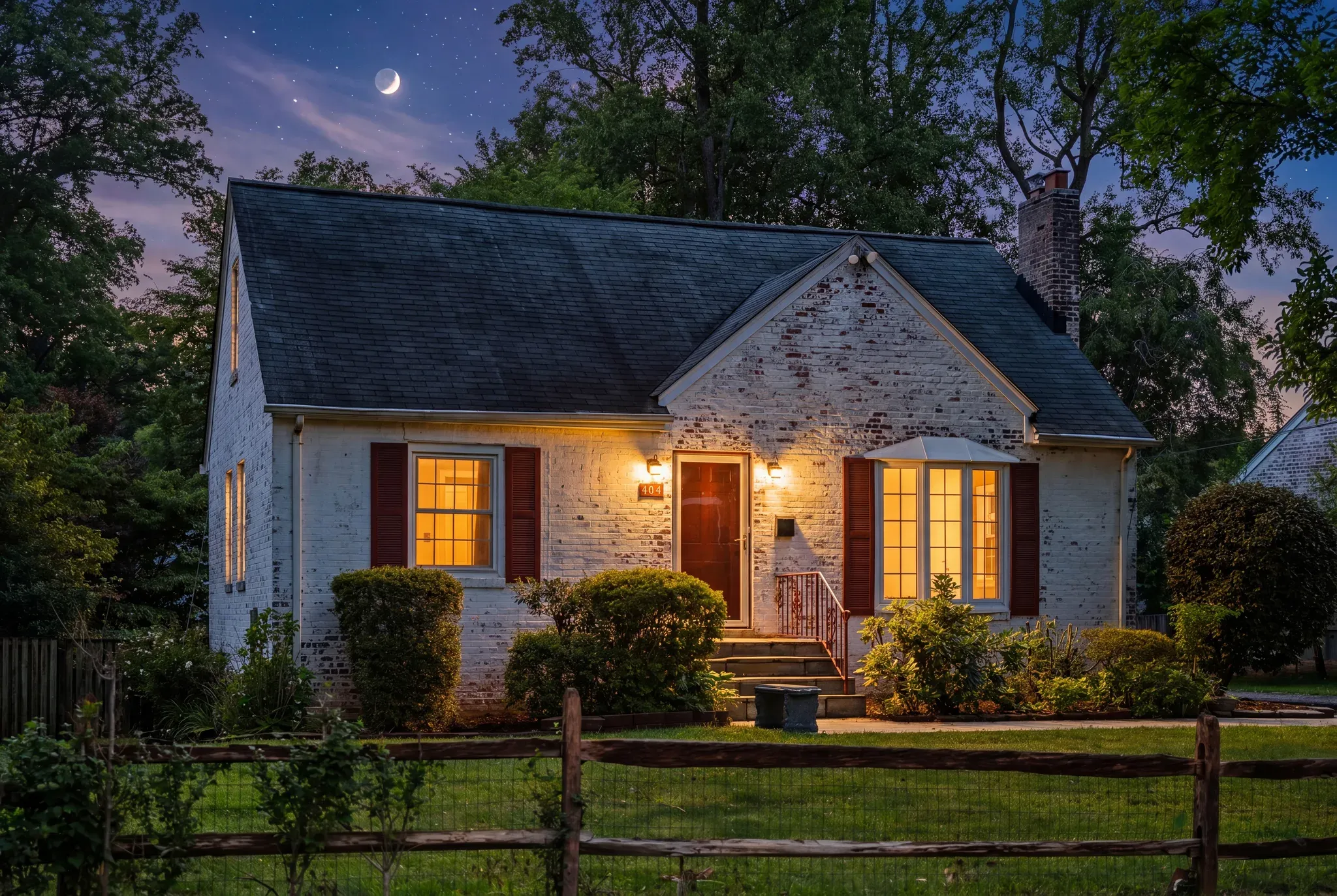 Twilight exterior photo of a whitewashed brick cottage with warmly lit windows — real estate listing photography for agents by Umedia