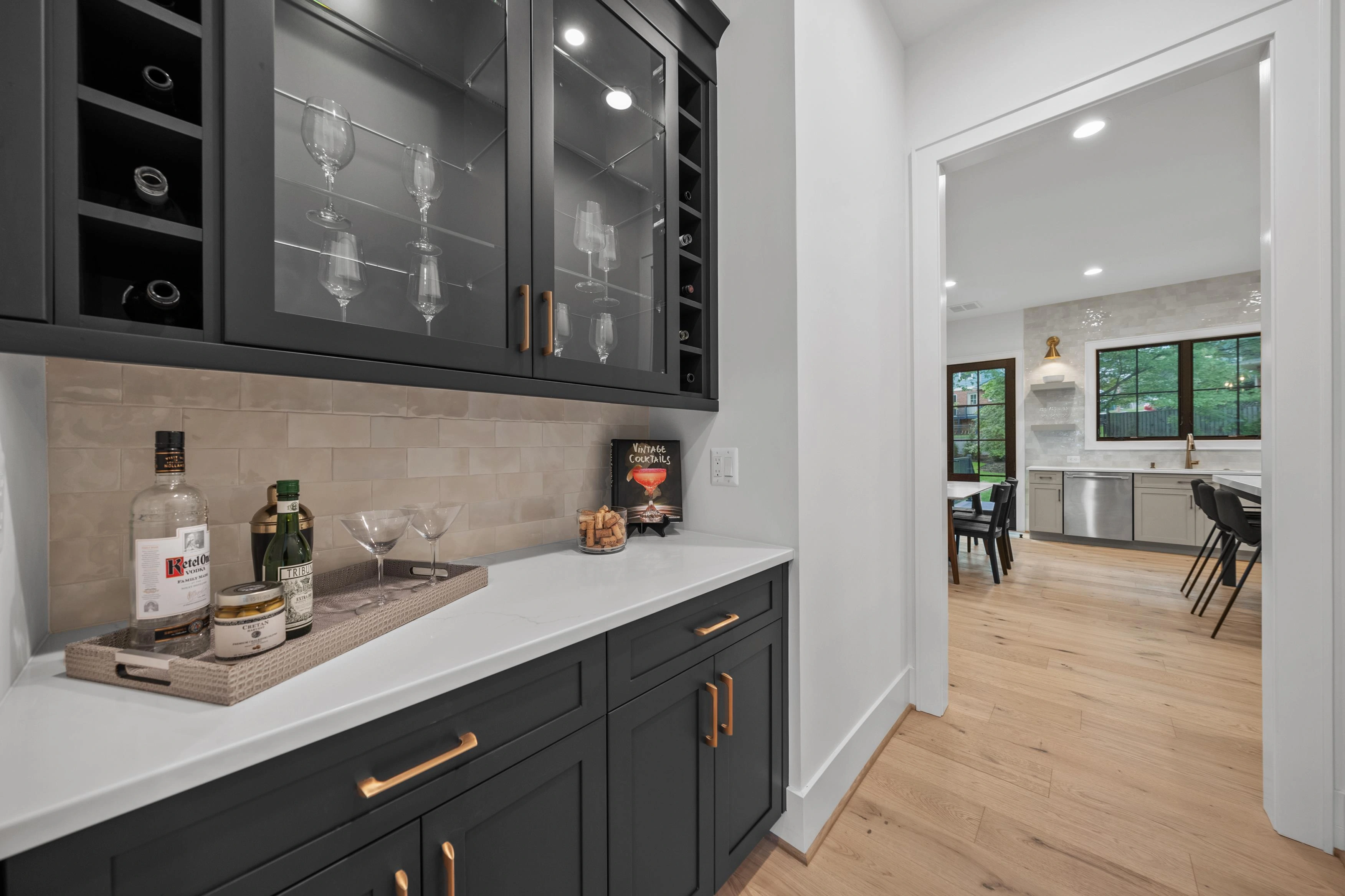 Butler pantry with dark cabinetry, glass-front wine storage, and gold hardware