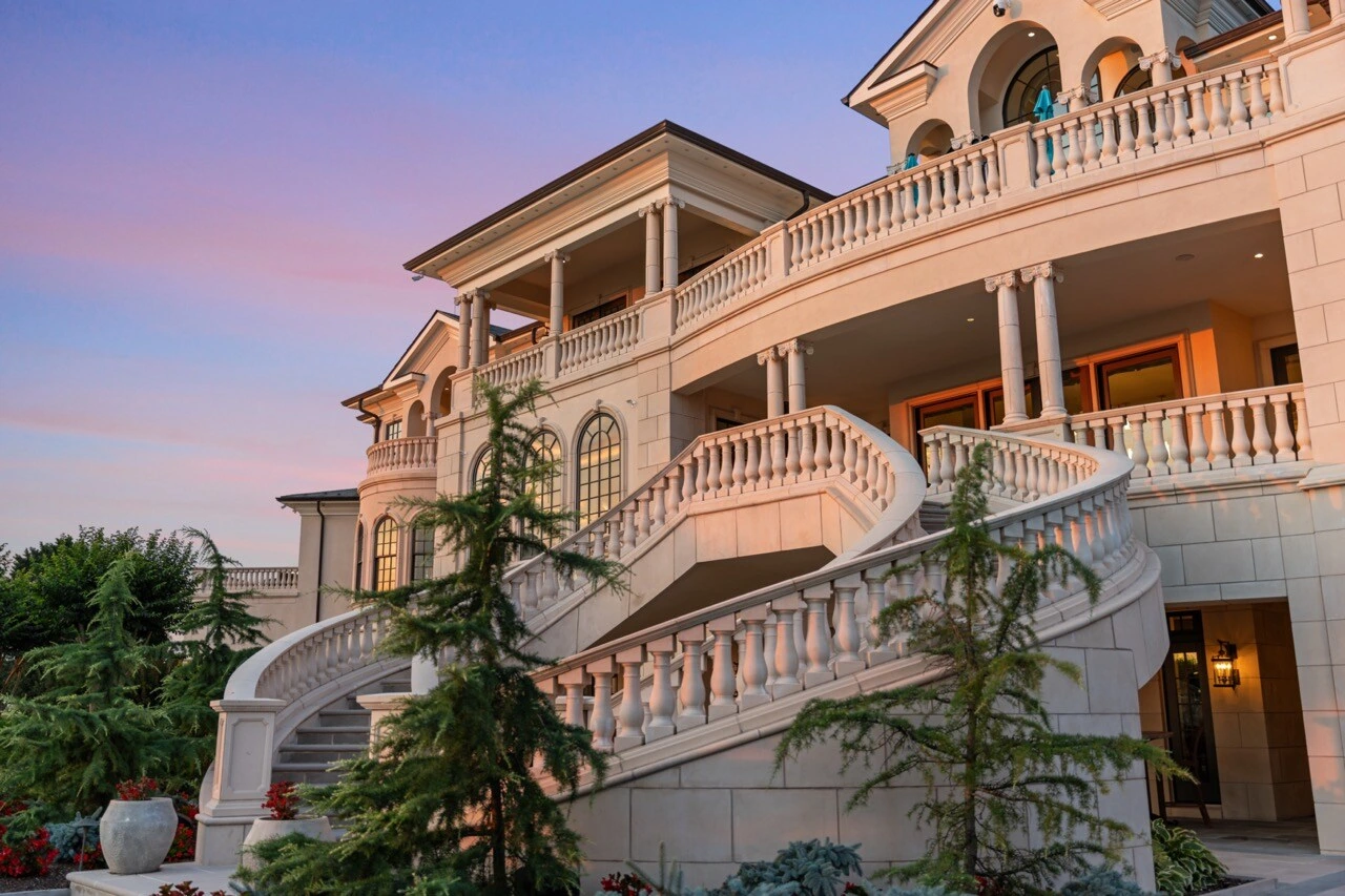 Luxury mansion exterior at sunset with illuminated windows and curved stone staircase