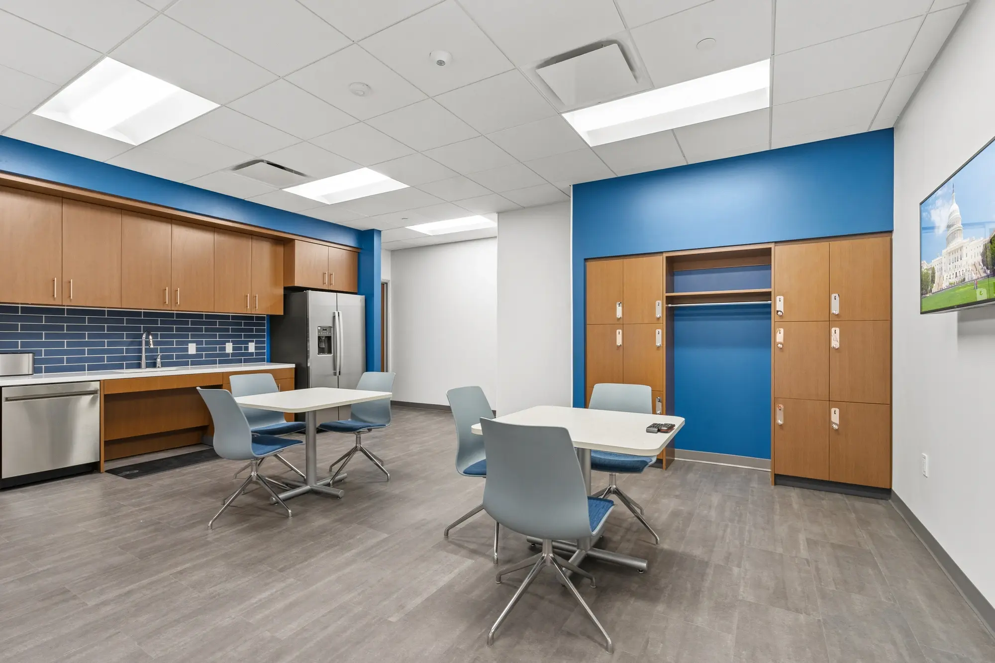 Employee break room with blue subway tile backsplash, oak cabinetry, stainless appliances, dining tables, personal lockers, and Capitol photo