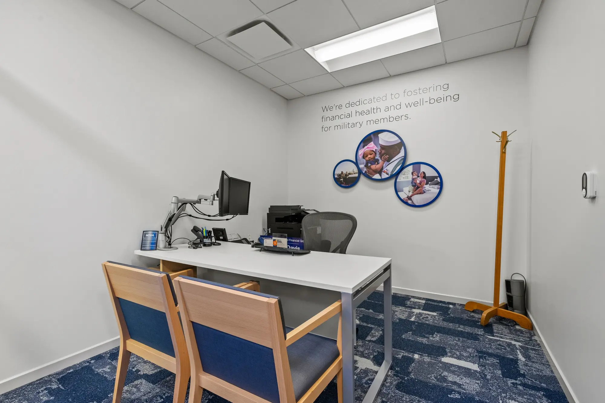 Private consultation room with military service wall text, circular photo displays, desk with monitor, and coat rack