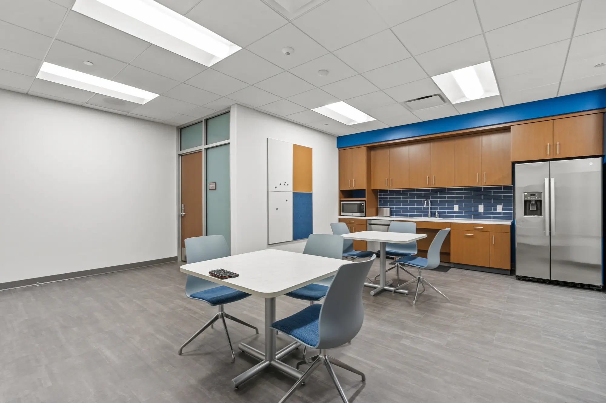 Break room alternate view with blue tile kitchen, oak cabinets, stainless steel refrigerator, microwave, and dining tables