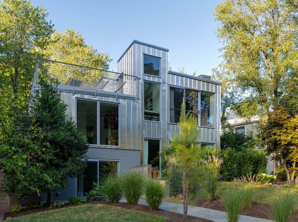 Multi-story modern house exterior with metal cladding surrounded by trees